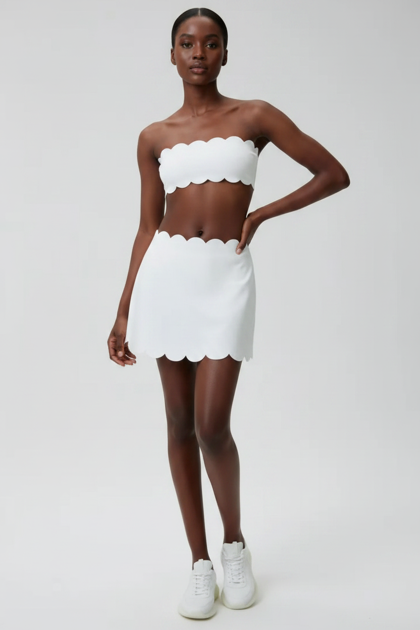Woman wearing a white scalloped top and skirt set on a plain background
