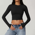 Person wearing a black long-sleeve crop top and blue jeans on a gray background